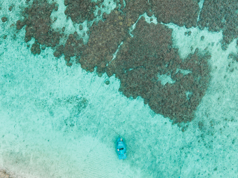 Aerial view of a lone boat adrift on turquoise waters contrasting with the rugged texture of the reef Vashafaru Island Thiladhummathi Atoll Maldives. Aerial view of a lone boat adrift on turquoise waters contrasting with the rugged texture of the reef Vashafaru Island Thiladhummathi Atoll Maldives.