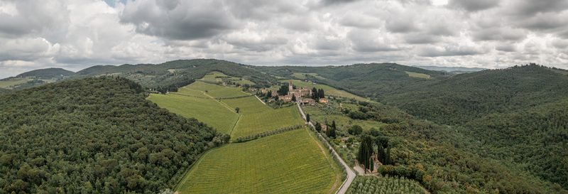Aerial view of the historic Badia a Passignano abbey surrounded by lush green vineyards rolling hills and cypress trees under a cloudy sky in Passignano Toscana Italy. Aerial view of the historic Badia a Passignano abbey surrounded by lush green vineyards rolling hills and cypress trees under a cloudy sky in Passignano Toscana Italy.