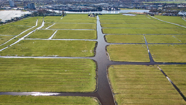 Aerial view of a verdant landscape where stripes of green fields meet with the dark blue canals creating a mesmerizing contrast Wormer Netherlands. Aerial view of a verdant landscape where stripes of green fields meet with the dark blue canals creating a mesmerizing contrast Wormer Netherlands.
