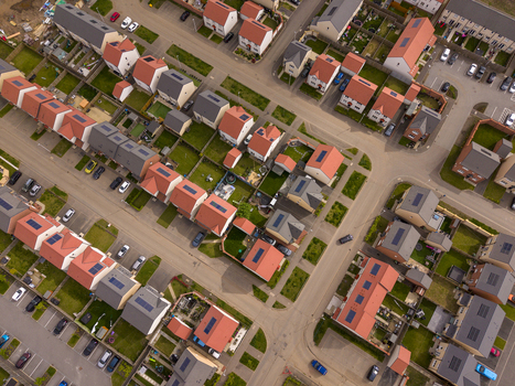 Aerial view of a modern residential neighborhood featuring rows of houses with red and grey roofs solar panels and private gardens in Edinburgh Scotland United Kingdom.