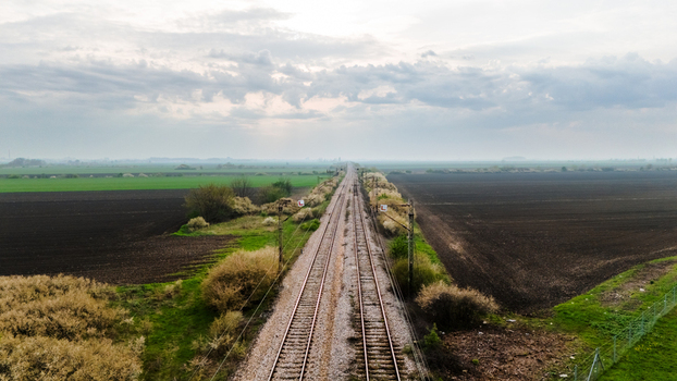 Aerial view of railway tracks cutting through contrasting fields of vibrant green and dark soil under a soft diffused sky Sremska Mitrovica Vojvodina Serbia. Aerial view of railway tracks cutting through contrasting fields of vibrant green and dark soil under a soft diffused sky Sremska Mitrovica Vojvodina Serbia.