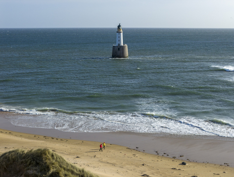 Aerial view of Rattray Head Lighthouse in the North Sea with waves crashing and people walking on the sandy beach in Peterhead Scotland United Kingdom. Aerial view of Rattray Head Lighthouse in the North Sea with waves crashing and people walking on the sandy beach in Peterhead Scotland United Kingdom.