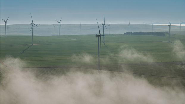 Aerial view of wind turbines in a wind farm surrounded by green fields and morning mist in Vredenburg Western Cape South Africa. Aerial view of wind turbines in a wind farm surrounded by green fields and morning mist in Vredenburg Western Cape South Africa.
