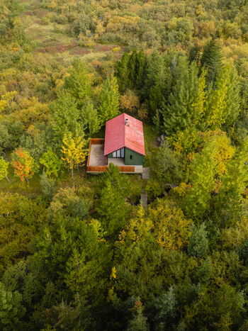 Aerial view of a solitary cabin with a striking red roof nestled amidst a dense vibrant forest of green and gold Egilsstaðir Fljótsdalshreppur Iceland. Aerial view of a solitary cabin with a striking red roof nestled amidst a dense vibrant forest of green and gold Egilsstaðir Fljótsdalshreppur Iceland.