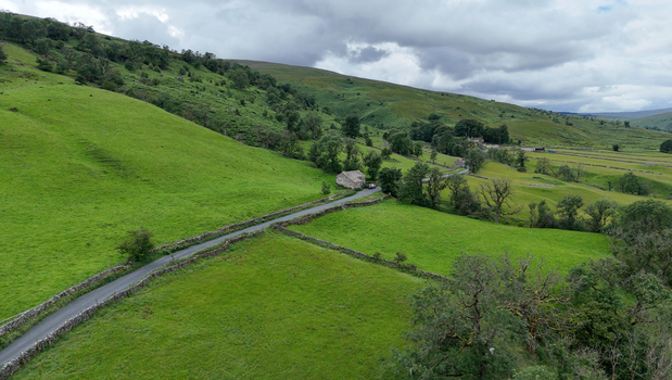 View of the rolling green hills and traditional dry stone walls along a winding country road in Hawes England United Kingdom. View of the rolling green hills and traditional dry stone walls along a winding country road in Hawes England United Kingdom.