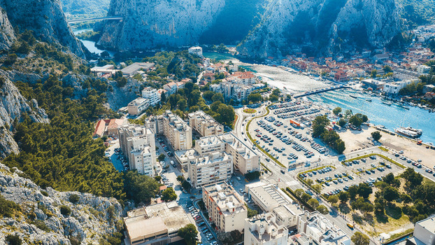 Aerial view of the town of Omis featuring residential buildings a parking area and the Cetina River flowing between dramatic limestone cliffs in Omis Split Dalmatia County Croatia. Aerial view of the town of Omis featuring residential buildings a parking area and the Cetina River flowing between dramatic limestone cliffs in Omis Split Dalmatia County Croatia.