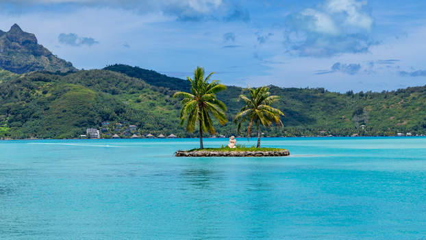 View of a small island with palm trees in the turquoise lagoon of Bora Bora Leeward Islands French Polynesia.