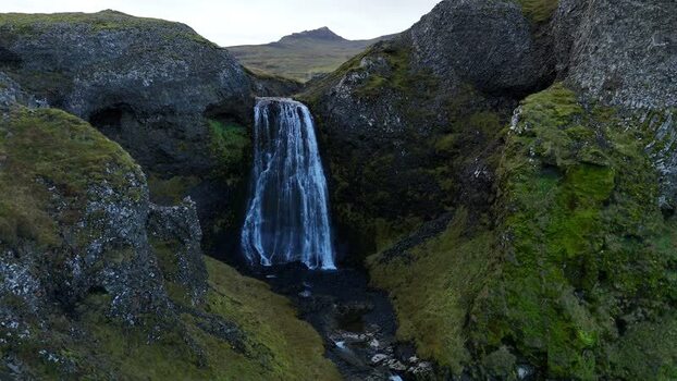 Aerial view of Bugsfoss waterfall between mossy cliffs Iceland.