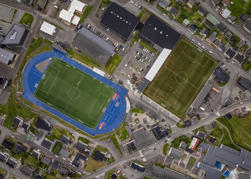 Aerial view of Djupumyra Stadium featuring football pitches and an athletic track surrounded by urban buildings and streets in Klaksvik Northern Isles Faroe Islands.