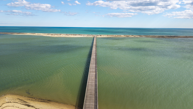 Aerial view of a long wooden bridge stretching across the turquoise waters connecting sandy shores under a sky of gentle clouds Duxbury Massachusetts United States.
