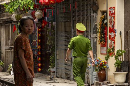 Hanoi Ha Noi Vietnam 11 November 2025 View of an elderly woman and a police officer in uniform walking past a house decorated with red lanterns and flags in a narrow street.