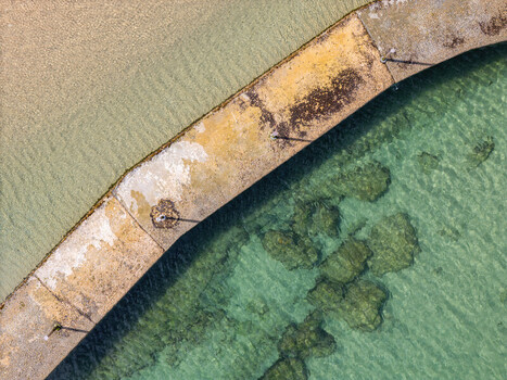 Aerial view of a curved concrete pier separating sandy shallows from clear turquoise water with visible rocks Cascais Lisbon Portugal. Aerial view of a curved concrete pier separating sandy shallows from clear turquoise water with visible rocks Cascais Lisbon Portugal.