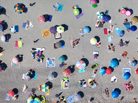 Aerial view of a crowded public beach with colorful umbrellas beach towels and people relaxing on the sand at the coast of Bergeggi Liguria Italy.
