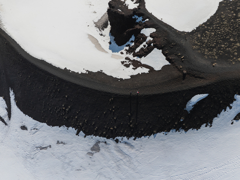 Aerial view of the volcanic crater rim on the south side of Mount Etna with black ash patches of white snow and a hiker standing on the edge in Nicolosi Sicilia Italy. Aerial view of the volcanic crater rim on the south side of Mount Etna with black ash patches of white snow and a hiker standing on the edge in Nicolosi Sicilia Italy.