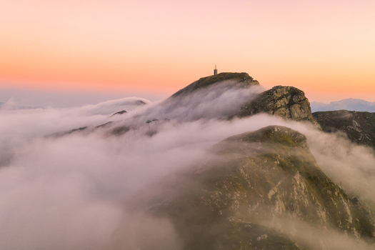 Aerial view of the mountain peaks of Cerreto Laghi surrounded by a thick sea of clouds under a soft pink sunset sky Cerreto Laghi Emilia Romagna Italy. Aerial view of the mountain peaks of Cerreto Laghi surrounded by a thick sea of clouds under a soft pink sunset sky Cerreto Laghi Emilia Romagna Italy.