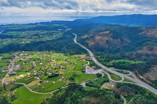 Aerial view of the Autovia del Cantabrico highway winding through lush green hills and rural villages under a cloudy sky Cudillero Asturias Spain.