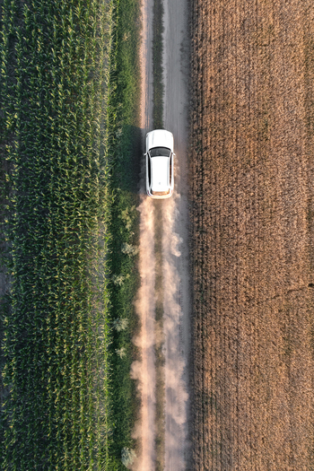 Aerial view of a white car kicking up dust as it speeds down a rural road between fields of green and brown Chyhyryns kyi district Cherkasy Oblast Ukraine. Aerial view of a white car kicking up dust as it speeds down a rural road between fields of green and brown Chyhyryns kyi district Cherkasy Oblast Ukraine.