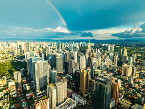 Aerial view of the dense Makati skyline featuring modern skyscrapers under a vibrant rainbow and blue sky with scattered clouds Makati City Metro Manila Philippines.