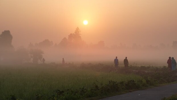 View of sunrise over rural fields with people walking in Bangladesh.