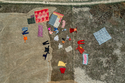 Aerial view of colorful clothes textiles and garments spread out on a large net and dry grass to dry in the sun Bogura Rajshahi Division Bangladesh.