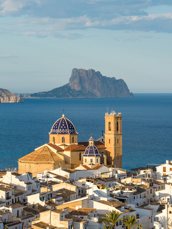 Aerial view of the Church of Our Lady of Consolation with blue tiled domes above white buildings overlooking the Mediterranean Sea and Penon de Ifach in Altea Valencian Community Spain.