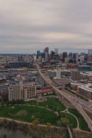 Aerial view of the Denver skyline featuring modern skyscrapers urban infrastructure a green park area and a river under a cloudy sky in Denver Colorado United States. Aerial view of the Denver skyline featuring modern skyscrapers urban infrastructure a green park area and a river under a cloudy sky in Denver Colorado United States.