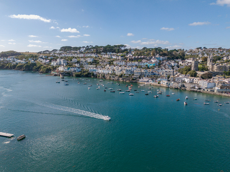 Aerial view of the Fowey river featuring numerous small boats moored near the historic town of Fowey with its hillside houses and lush greenery in Fowey Cornwall United Kingdom. Aerial view of the Fowey river featuring numerous small boats moored near the historic town of Fowey with its hillside houses and lush greenery in Fowey Cornwall United Kingdom.