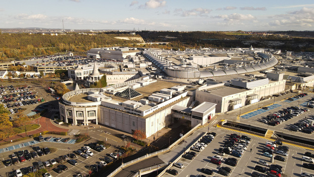 Aerial view of the Bluewater shopping centre featuring its distinctive curved architecture extensive parking lots and surrounding landscape in Dartford England United Kingdom. Aerial view of the Bluewater shopping centre featuring its distinctive curved architecture extensive parking lots and surrounding landscape in Dartford England United Kingdom.