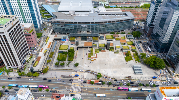 Aerial view of Busan Station featuring a modern glass facade a landscaped plaza with green spaces and surrounding high rise buildings and traffic in Busan Busan South Korea. Aerial view of Busan Station featuring a modern glass facade a landscaped plaza with green spaces and surrounding high rise buildings and traffic in Busan Busan South Korea.
