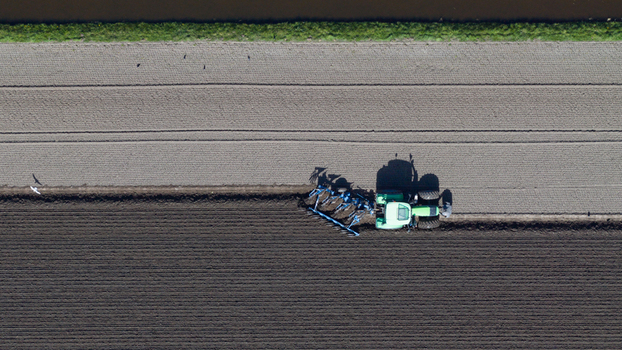 Aerial view of a green tractor plowing a field with dark soil and birds flying nearby Heiloo North Holland Netherlands. Aerial view of a green tractor plowing a field with dark soil and birds flying nearby Heiloo North Holland Netherlands.