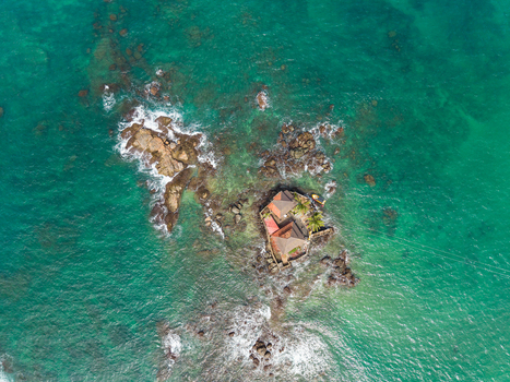 Aerial view of Seenigama Muhudu Dewalaya temple on a small rocky island surrounded by turquoise ocean water and waves crashing on the shore in Peraliya Sri Lanka. Aerial view of Seenigama Muhudu Dewalaya temple on a small rocky island surrounded by turquoise ocean water and waves crashing on the shore in Peraliya Sri Lanka.