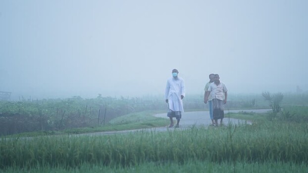 View of men walking on a rural path through foggy fields Bangladesh.