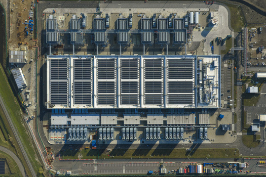 Aerial view of an AI data center with cooling towers and cloud computing hub exterior featuring industrial infrastructure and technical equipment. Aerial view of an AI data center with cooling towers and cloud computing hub exterior featuring industrial infrastructure and technical equipment.