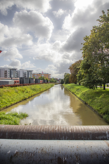 View of a calm canal lined with green grassy banks and modern architecture under a cloudy sky in Gdansk Pomeranian Voivodeship Poland. View of a calm canal lined with green grassy banks and modern architecture under a cloudy sky in Gdansk Pomeranian Voivodeship Poland.