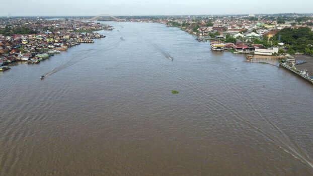 Aerial view of the Musi River with the Ampera Bridge in the distance surrounded by dense urban housing and boats in Kecamatan Seberang Ulu I Sumatera Selatan Indonesia. Aerial view of the Musi River with the Ampera Bridge in the distance surrounded by dense urban housing and boats in Kecamatan Seberang Ulu I Sumatera Selatan Indonesia.