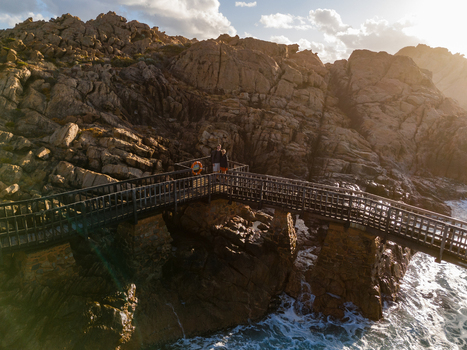 Aerial view of Canal Rocks Bridge with a couple standing on the wooden walkway surrounded by rugged coastal rock formations and crashing waves in Yallingup Western Australia Australia. Aerial view of Canal Rocks Bridge with a couple standing on the wooden walkway surrounded by rugged coastal rock formations and crashing waves in Yallingup Western Australia Australia.