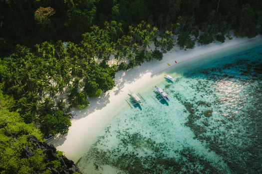 Aerial view of Papaya Beach with white sand lush palm trees and traditional outrigger boats floating in clear turquoise water El Nido Mimaropa Philippines. Aerial view of Papaya Beach with white sand lush palm trees and traditional outrigger boats floating in clear turquoise water El Nido Mimaropa Philippines.