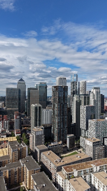 London United Kingdom 16 June 2026 Aerial view of the Canary Wharf financial district featuring modern skyscrapers glass office towers and residential buildings under a blue sky.