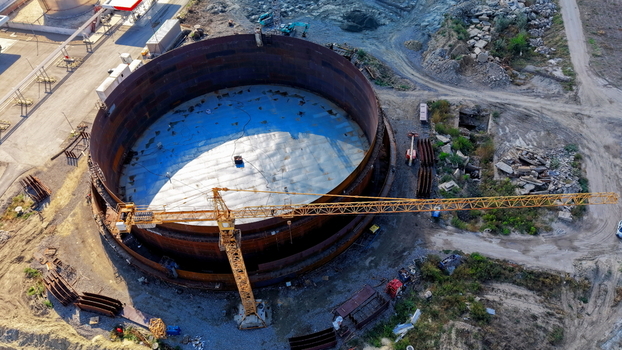 Aerial view of a large industrial fuel tank under construction with a yellow tower crane positioned alongside the circular steel structure in Kovin Vojvodina Serbia. Aerial view of a large industrial fuel tank under construction with a yellow tower crane positioned alongside the circular steel structure in Kovin Vojvodina Serbia.