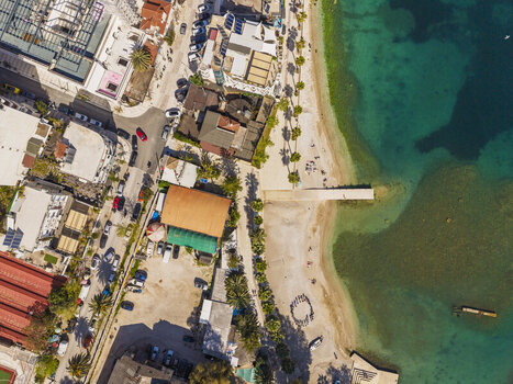 Aerial view of Saranda beach with a pier palm trees and coastal buildings along the clear turquoise waters of the Ionian Sea in Saranda Vlore County Albania. Aerial view of Saranda beach with a pier palm trees and coastal buildings along the clear turquoise waters of the Ionian Sea in Saranda Vlore County Albania.
