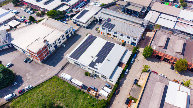 Aerial view of an industrial production area featuring warehouses with solar panels on rooftops parking lots with vehicles and surrounding urban infrastructure in Milan Lombardy Italy.