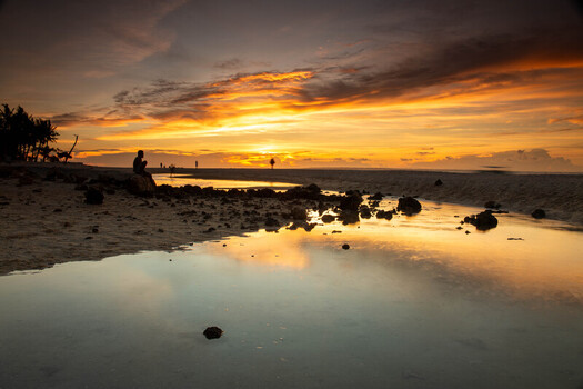 View of Bantayan Island at sunset with a person sitting on a rock by the tide pools reflecting the golden sky on the sandy beach in Cebu Central Visayas Philippines. View of Bantayan Island at sunset with a person sitting on a rock by the tide pools reflecting the golden sky on the sandy beach in Cebu Central Visayas Philippines.