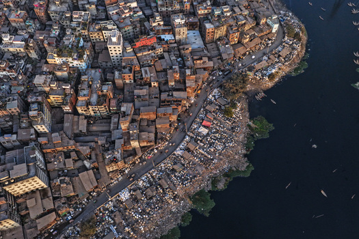 Aerial view of Buriganga River flowing past dense urban buildings narrow streets and boats along the riverbank in Dhaka Dhaka Division Bangladesh. Aerial view of Buriganga River flowing past dense urban buildings narrow streets and boats along the riverbank in Dhaka Dhaka Division Bangladesh.