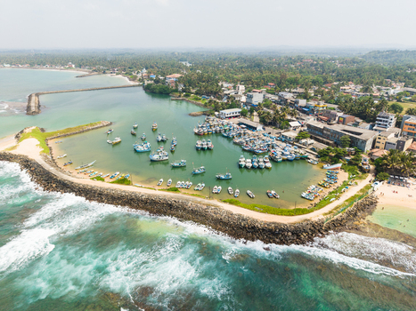 Aerial view of fishing boats moored in a sheltered harbor protected by a stone breakwater along the tropical coastline Hikkaduwa Southern Province Sri Lanka. Aerial view of fishing boats moored in a sheltered harbor protected by a stone breakwater along the tropical coastline Hikkaduwa Southern Province Sri Lanka.