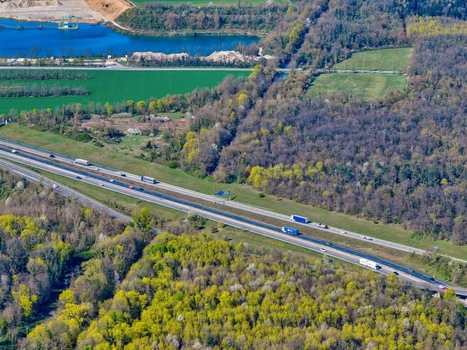 Aerial view of a highway cutting through lush forests and open fields with a quarry lake reflecting the sky Sausheim Grand Est France.
