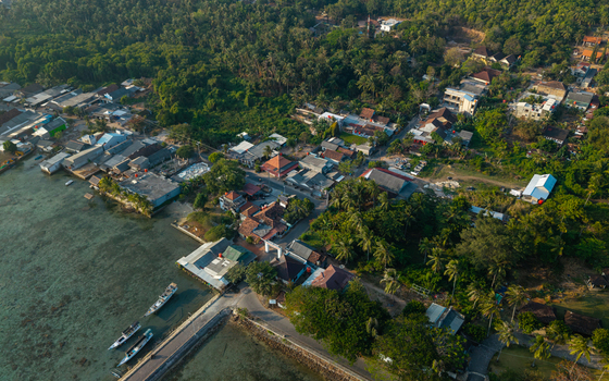 Aerial view of Karimunjawa village with traditional houses lush tropical trees and boats docked along the clear coastal waters in Karimunjawa Central Java Indonesia. Aerial view of Karimunjawa village with traditional houses lush tropical trees and boats docked along the clear coastal waters in Karimunjawa Central Java Indonesia.