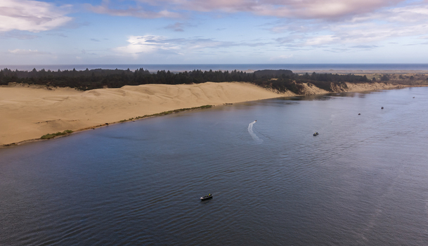 Aerial view of salmon fishing boats navigating the Siuslaw River near the expansive sand dunes and coastal forest Florence Oregon United States. Aerial view of salmon fishing boats navigating the Siuslaw River near the expansive sand dunes and coastal forest Florence Oregon United States.