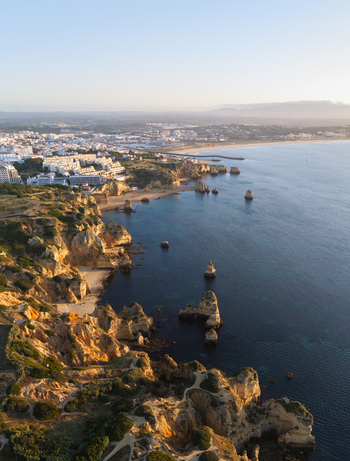 Aerial view of the rugged coastline and golden cliffs of Lagos with sandy beaches turquoise waters and the town skyline in the background Lagos Faro District Portugal.