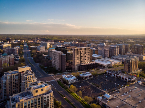 Reston United States 12 April 2020 Aerial view of the modern urban skyline and commercial district with office buildings parking lots and roads during the golden hour.