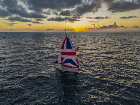 Aerial view of a sailboat with a Union Jack patterned sail gliding across the dark blue ocean during a golden sunset Waimea Hawaii United States. Aerial view of a sailboat with a Union Jack patterned sail gliding across the dark blue ocean during a golden sunset Waimea Hawaii United States.
